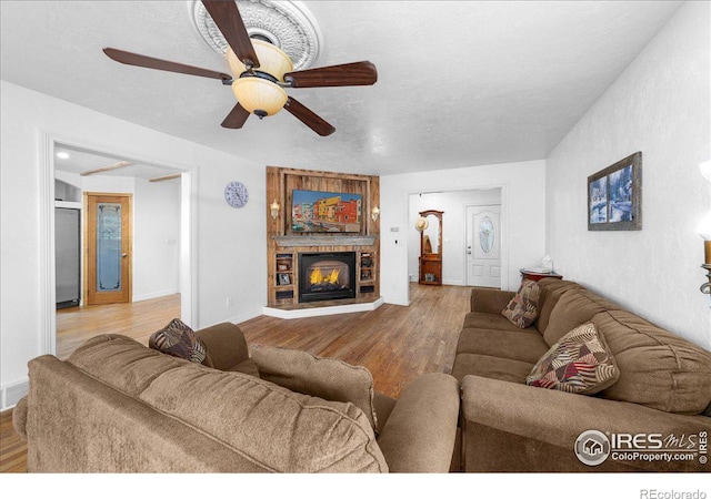 living room featuring a fireplace, a textured ceiling, light wood-type flooring, and ceiling fan