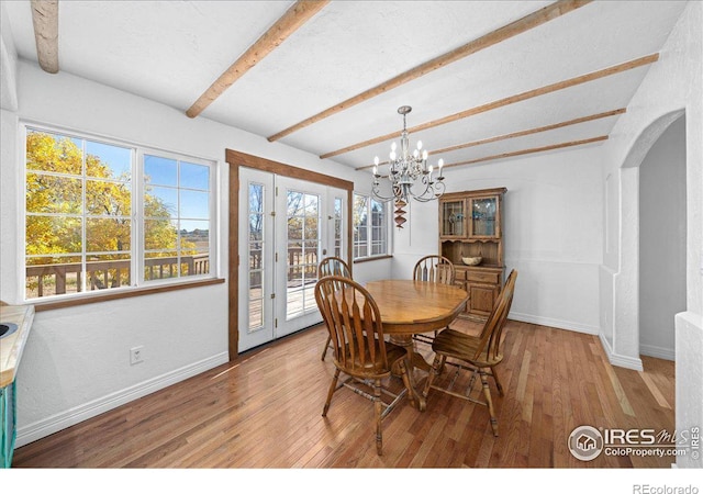 dining space with beam ceiling, light hardwood / wood-style flooring, and an inviting chandelier