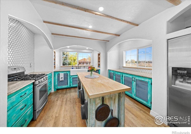 kitchen with beamed ceiling, light wood-type flooring, a textured ceiling, and stainless steel gas range