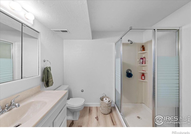 bathroom with walk in shower, vanity, a textured ceiling, wood-type flooring, and toilet