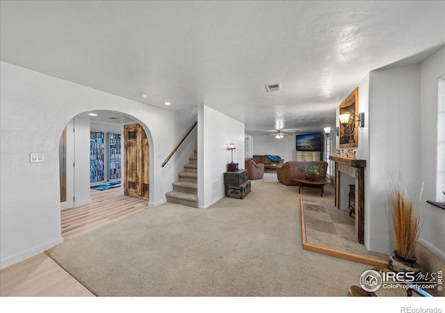 living room with a tiled fireplace, light carpet, ceiling fan, and a textured ceiling