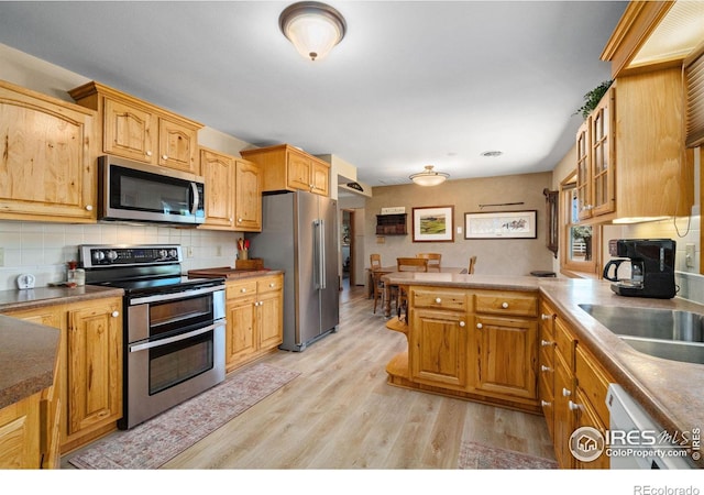 kitchen featuring appliances with stainless steel finishes, sink, backsplash, light hardwood / wood-style floors, and kitchen peninsula