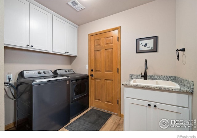 laundry area featuring washer and dryer, sink, cabinets, and light wood-type flooring