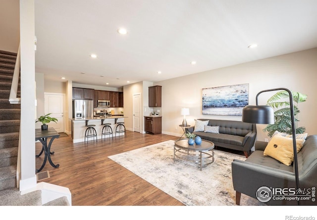 living area with recessed lighting, dark wood-type flooring, visible vents, baseboards, and stairs