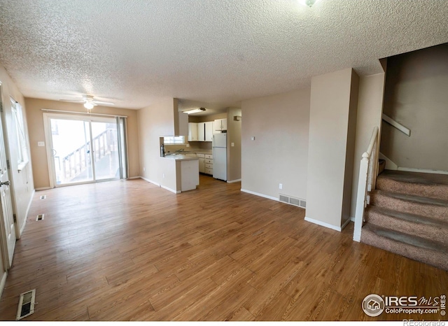 unfurnished living room with ceiling fan, light hardwood / wood-style floors, and a textured ceiling