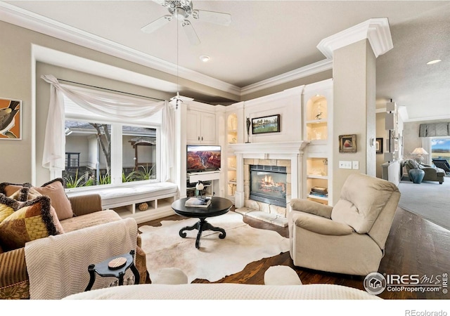 living room featuring a tile fireplace, ceiling fan, crown molding, and dark wood-type flooring