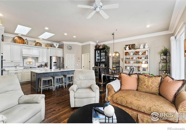 living room featuring a skylight, sink, dark wood-type flooring, ceiling fan with notable chandelier, and ornamental molding