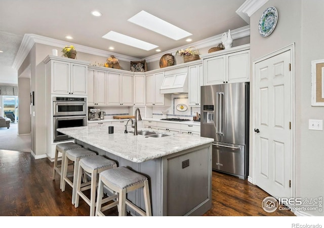 kitchen with a skylight, stainless steel appliances, sink, a center island with sink, and white cabinetry