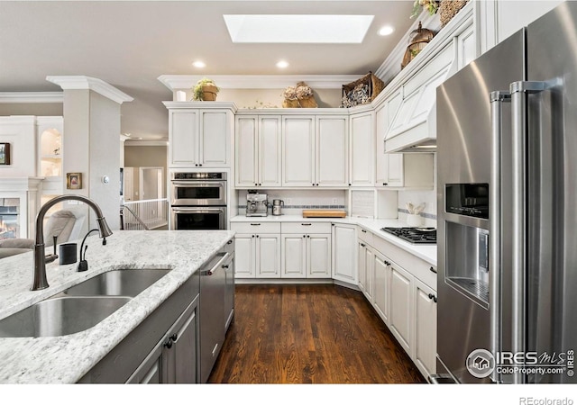 kitchen featuring sink, a skylight, light stone countertops, appliances with stainless steel finishes, and white cabinetry