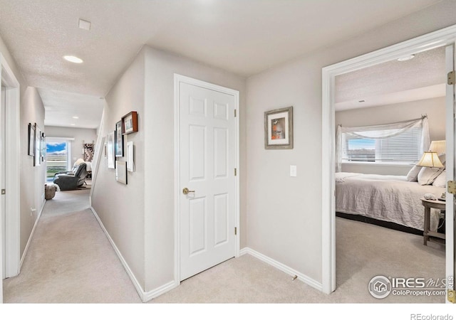 hallway with light carpet, a textured ceiling, and plenty of natural light