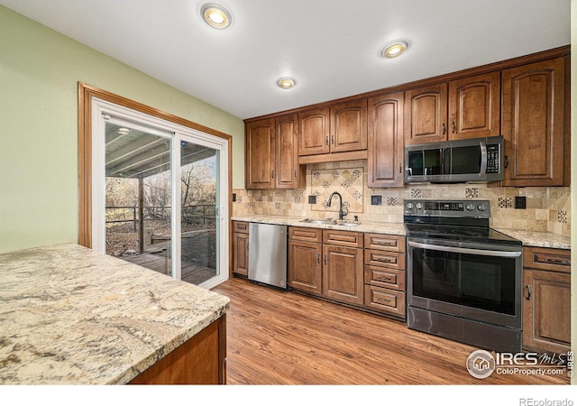 kitchen with light hardwood / wood-style floors, light stone counters, sink, and appliances with stainless steel finishes