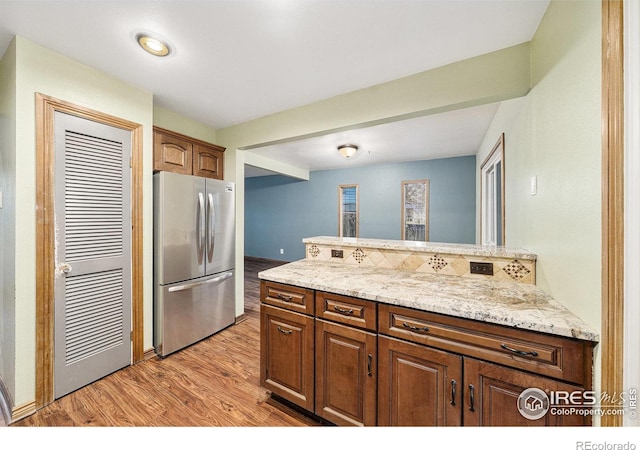 kitchen featuring stainless steel fridge, light hardwood / wood-style flooring, and light stone countertops