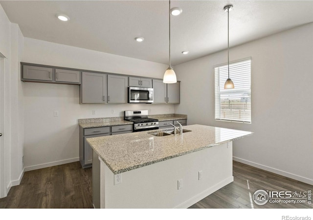 kitchen with a center island with sink, sink, light stone countertops, decorative light fixtures, and stainless steel appliances