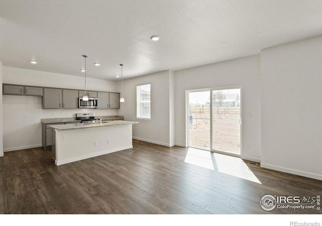 kitchen featuring stainless steel appliances, hanging light fixtures, a center island with sink, and gray cabinetry