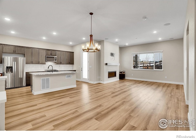 kitchen featuring light hardwood / wood-style floors, pendant lighting, a kitchen island with sink, dark brown cabinets, and appliances with stainless steel finishes