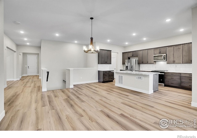 kitchen featuring dark brown cabinetry, stainless steel appliances, pendant lighting, a kitchen island with sink, and light wood-type flooring