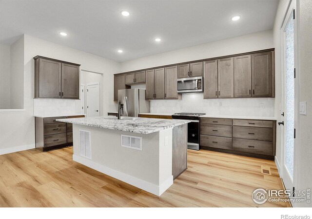 kitchen featuring tasteful backsplash, light hardwood / wood-style flooring, an island with sink, dark brown cabinets, and appliances with stainless steel finishes