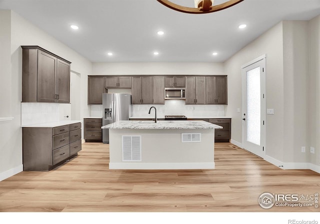 kitchen with a center island with sink, dark brown cabinets, light hardwood / wood-style floors, and stainless steel appliances