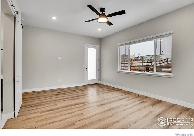 unfurnished room with light wood-type flooring, a barn door, and ceiling fan