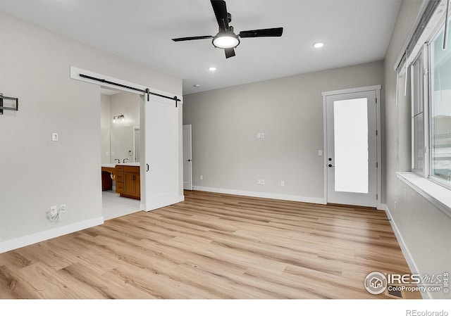 unfurnished room featuring ceiling fan, a barn door, and light hardwood / wood-style floors