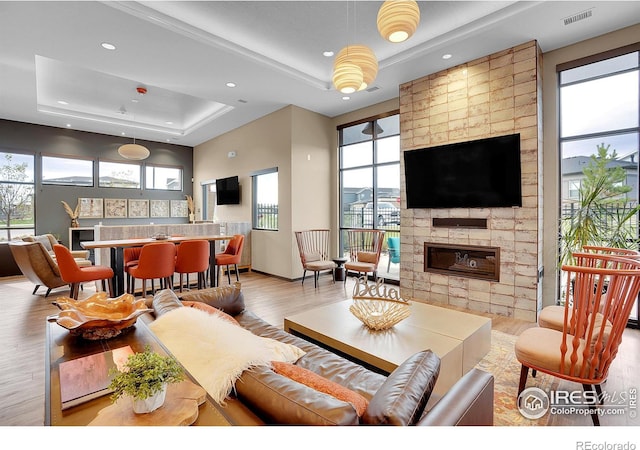 living room featuring a fireplace, a tray ceiling, plenty of natural light, and light hardwood / wood-style floors