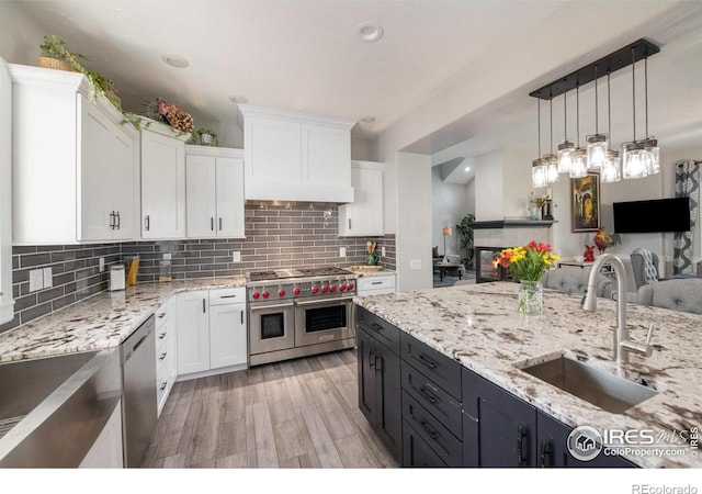 kitchen with stainless steel appliances, sink, pendant lighting, white cabinets, and light hardwood / wood-style floors