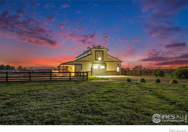 back house at dusk with a rural view, an outdoor structure, and a lawn