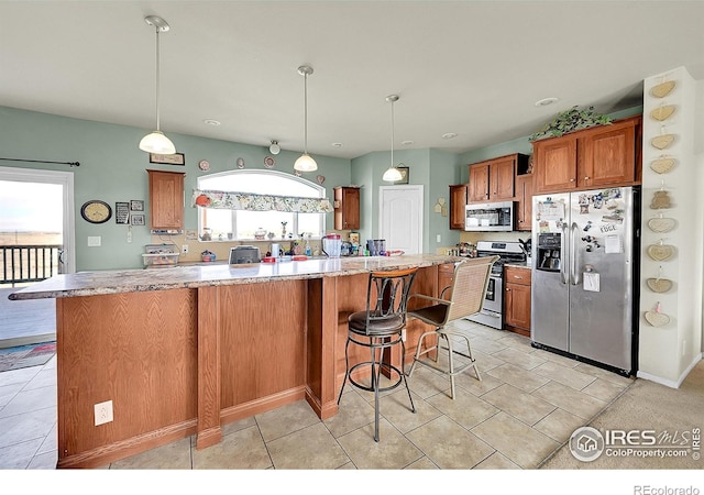 kitchen featuring a breakfast bar, light tile patterned floors, appliances with stainless steel finishes, decorative light fixtures, and a kitchen island