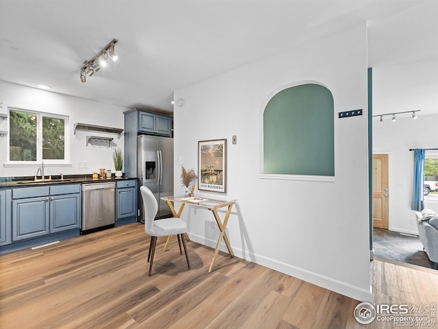 kitchen featuring appliances with stainless steel finishes, rail lighting, blue cabinets, sink, and light hardwood / wood-style flooring