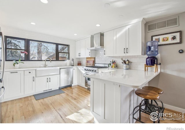 kitchen featuring kitchen peninsula, white cabinetry, wall chimney exhaust hood, and appliances with stainless steel finishes