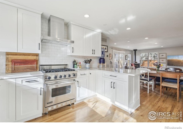 kitchen featuring kitchen peninsula, premium stove, white cabinets, and wall chimney range hood