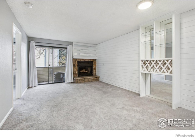 unfurnished living room featuring a stone fireplace, light colored carpet, a textured ceiling, and wooden walls