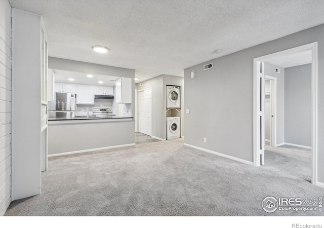 unfurnished living room featuring light colored carpet, stacked washing maching and dryer, and a textured ceiling