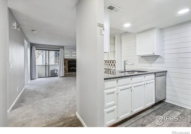 kitchen featuring carpet, dishwasher, sink, a fireplace, and white cabinetry