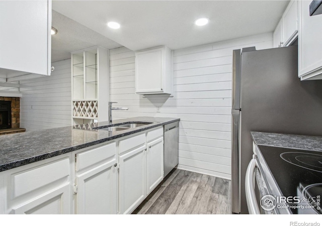 kitchen with sink, light hardwood / wood-style flooring, dark stone counters, a fireplace, and white cabinets