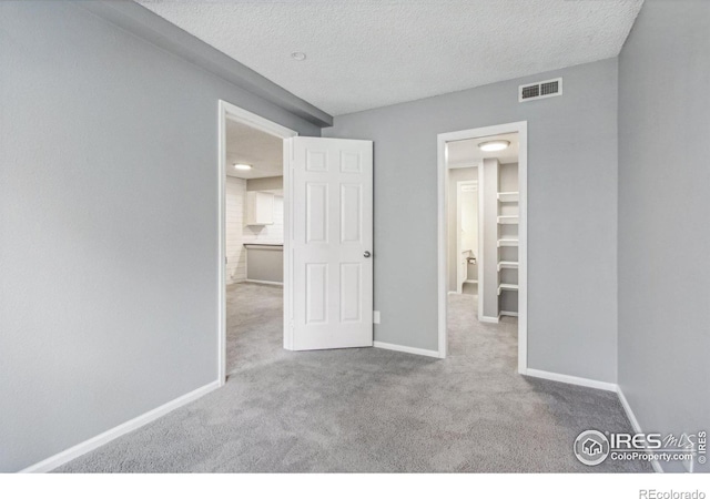 unfurnished bedroom with light carpet, a textured ceiling, and a walk in closet