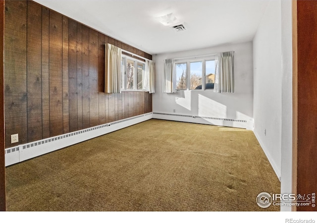 empty room with carpet, wooden walls, and a baseboard heating unit