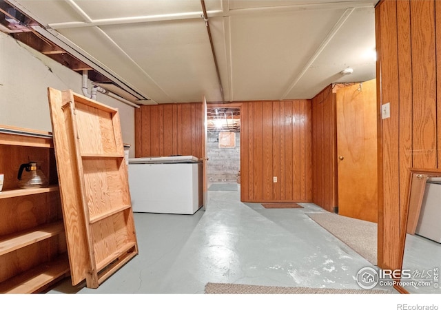 basement featuring fridge and wood walls