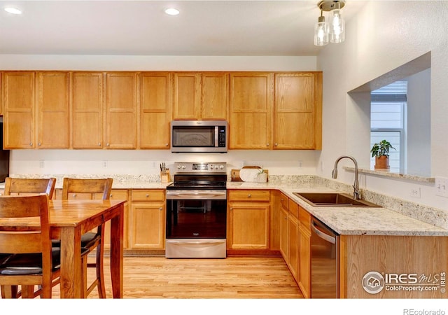 kitchen with light stone countertops, sink, kitchen peninsula, appliances with stainless steel finishes, and light wood-type flooring