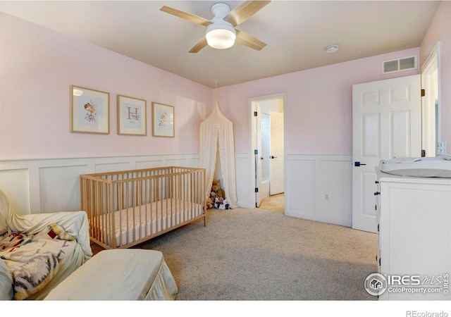 bedroom with ceiling fan, light colored carpet, and a nursery area