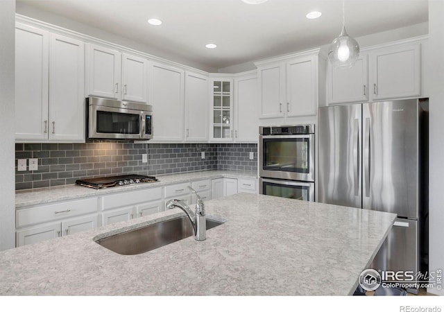 kitchen featuring decorative backsplash, stainless steel appliances, sink, decorative light fixtures, and white cabinets