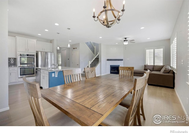 dining room with a fireplace, light hardwood / wood-style floors, sink, and ceiling fan with notable chandelier