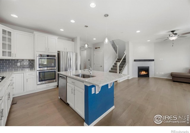 kitchen with a kitchen island with sink, a tile fireplace, sink, appliances with stainless steel finishes, and white cabinetry