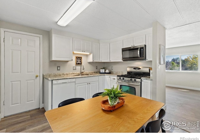 kitchen with a textured ceiling, stainless steel appliances, sink, white cabinets, and light hardwood / wood-style floors