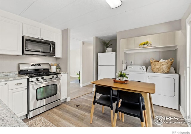 kitchen with white cabinetry, stainless steel appliances, light stone counters, washer and dryer, and light wood-type flooring