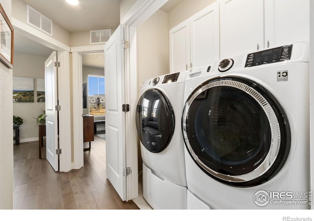 washroom with cabinet space, visible vents, wood finished floors, and washing machine and clothes dryer