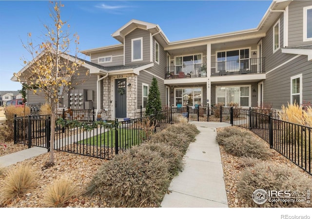 view of front facade featuring a balcony, stone siding, and a fenced front yard