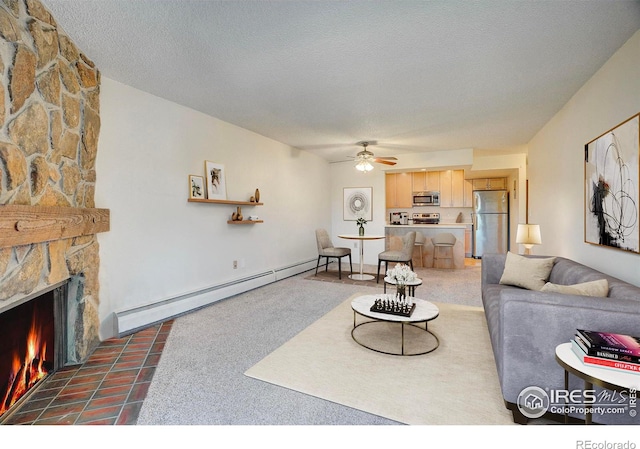 living room with a ceiling fan, a baseboard heating unit, a textured ceiling, and a stone fireplace