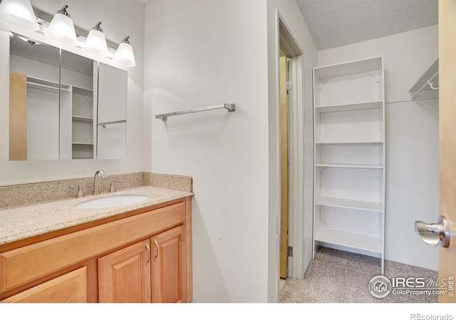 bathroom featuring a textured ceiling, a walk in closet, and vanity