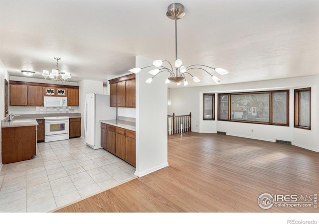 kitchen featuring hanging light fixtures, tasteful backsplash, a notable chandelier, white appliances, and light wood-type flooring